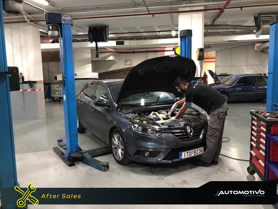 a man wearing a black t-shirt and grey pants fixing a dark gray renault car